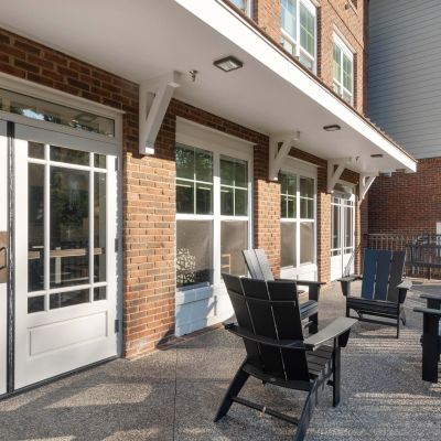 Black Adirondack lounge chairs arranged on a concrete patio outside a brick residential apartment building