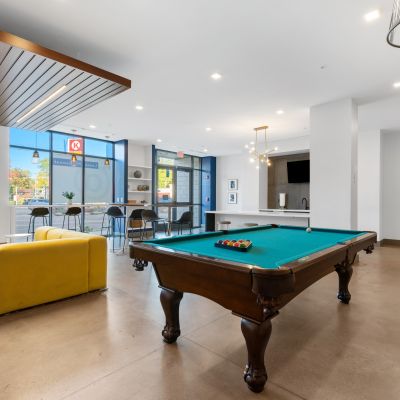 Modern apartment clubhouse lounge featuring a billiards pool table, a bright yellow sectional sofa, and resident bar seating