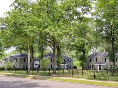 Shaded lawn and community buildings viewed behind a black perimeter fence at Bluff City Apartments in Memphis.