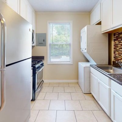 Galley kitchen with tile floors, white cabinets, stainless steel appliances, and a stacked washer and dryer at Bluff City Apartments in Memphis