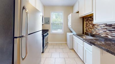 Galley kitchen with tile floors, white cabinets, stainless steel appliances, and a stacked washer and dryer at Bluff City Apartments in Memphis