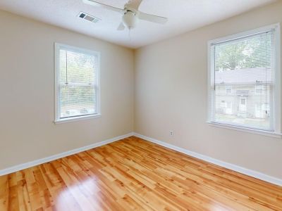 Unfurnished bedroom featuring natural hardwood flooring, beige walls, a ceiling fan, and bright windows at Bluff City Apartments in Memphis.