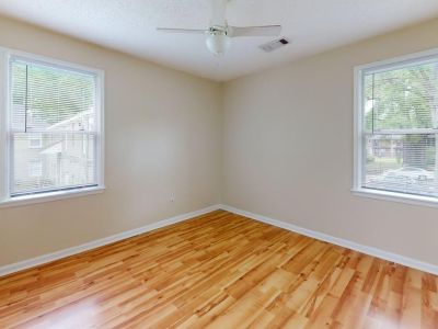 Empty apartment bedroom showcasing polished wood floors, a ceiling fan, and two windows providing natural light at Bluff City Apartments in Memphis