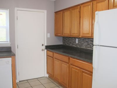 Kitchen interior featuring honey-oak wood cabinets, dark charcoal countertops, a white refrigerator, a white door, and neutral tile flooring at Center Court Apartments in Collierville, TN.