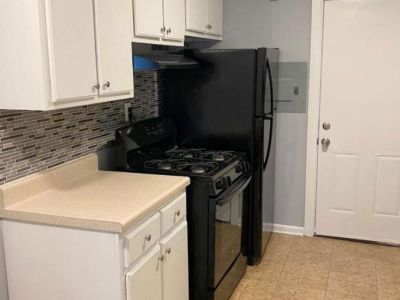 Updated kitchen space showcasing white cabinets, a black gas range stove, a black refrigerator, beige countertops, and a mosaic glass tile backsplash at Center Court Apartments in Collierville, TN.