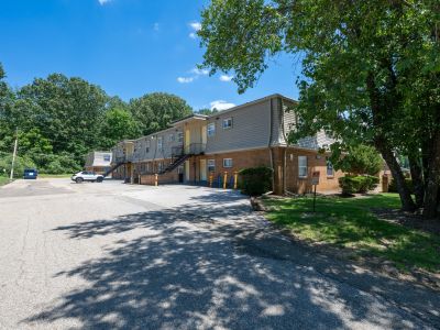 Exterior driving lane running alongside two-story residential buildings featuring brick lower levels, beige siding, and black iron staircases at Center Court Apartments in Collierville, TN.