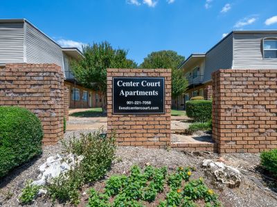 Property entrance monument sign built into a decorative brick wall, displaying the leasing phone number and website for Center Court Apartments in Collierville, TN.