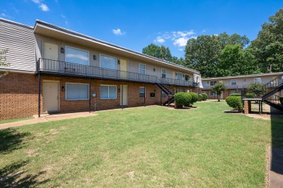 Angled view of a green grass courtyard lawn enclosed by multi-family two-story brick buildings with open walkways at Center Court Apartments in Collierville, TN.