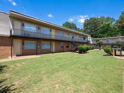 Angled view of a green grass courtyard lawn enclosed by multi-family two-story brick buildings with open walkways at Center Court Apartments in Collierville, TN.