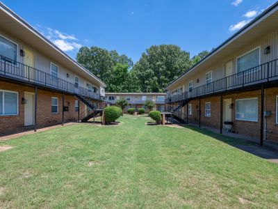 Symmetrical view looking down the middle of a wide green grass courtyard flanked by two-story brick and siding apartment wings at Center Court Apartments in Collierville, TN.