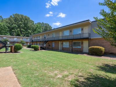 Courtyard perspective showing a well-maintained lawn, a partial view of a brick apartment building with upper balconies, and mature trees at Center Court Apartments in Collierville, TN.