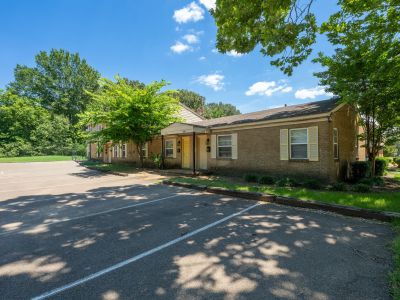 Exterior shot of a single-story brick building with yellow accent window shutters, located next to a freshly striped asphalt parking lot at Center Court Apartments in Collierville, TN.
