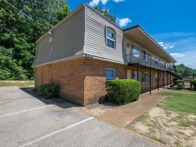 Corner profile of a multi-family building at building number 290, highlighting the brick exterior, mansard siding upper level, a concrete sidewalk with neat green hedges, and an adjacent parking lot at Center Court Apartments in Collierville, TN.