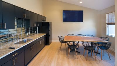 Resident clubhouse community room featuring a sleek kitchenette, a large live-edge wooden dining table, and a wall-mounted TV at Champion Hills apartments in Memphis.