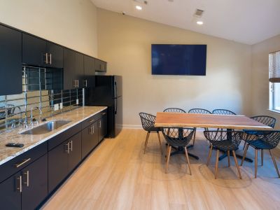 Resident clubhouse community room featuring a sleek kitchenette, a large live-edge wooden dining table, and a wall-mounted TV at Champion Hills apartments in Memphis.