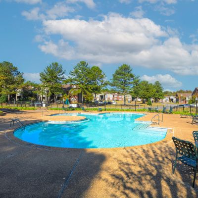 Large outdoor swimming pool and concrete sun deck with lounge chairs and patio tables at Champion Hills apartments in Memphis.