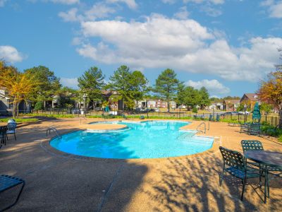 Large outdoor swimming pool and concrete sun deck with lounge chairs and patio tables at Champion Hills apartments in Memphis.