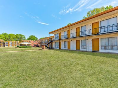 Two-story residential buildings with yellow doors and black railings facing a large green courtyard lawn at Cherry Creek apartments in Memphis.