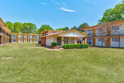 Exterior view of the single-story leasing office building surrounded by green grass and residential buildings at Cherry Creek apartments in Memphis.