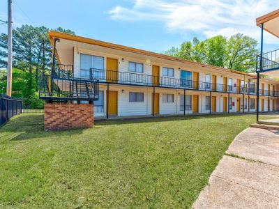 Exterior view of a long two-story residential building with white siding, exterior staircases, and a row of yellow doors at Cherry Creek apartments in Memphis.