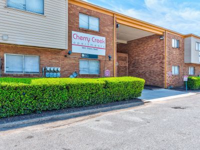 Exterior brick wall featuring the Cherry Creek apartments community sign above a manicured green hedge in Memphis.
