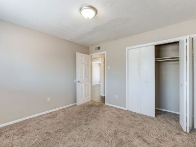 Empty apartment bedroom featuring neutral beige walls, plush carpeting, and a closet with white bifold doors at Cherry Creek in Memphis.