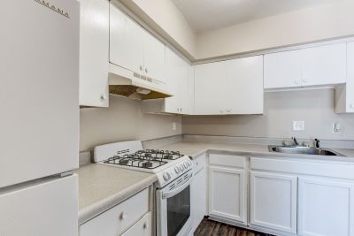 Apartment kitchen with white cabinetry, light countertops, a white gas range stove, and dark flooring at Cherry Creek apartments in Memphis.