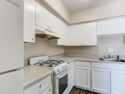 Apartment kitchen with white cabinetry, light countertops, a white gas range stove, and dark flooring at Cherry Creek apartments in Memphis.