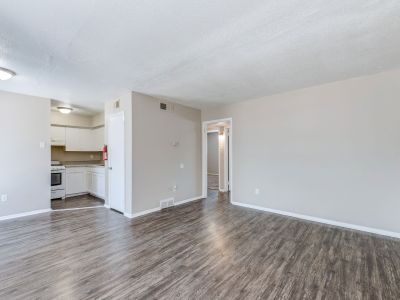 Open-concept living room with dark wood-look vinyl plank flooring and neutral walls leading toward the kitchen at Cherry Creek apartments in Memphis.