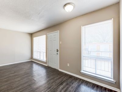 Interior living space showcasing dark wood-style flooring, a white front entry door, and large windows with blinds at Cherry Creek apartments in Memphis.