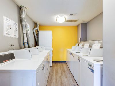 On-site community laundry facility equipped with multiple white washing machines and dryers against a bright yellow accent wall at Cherry Creek apartments in Memphis.