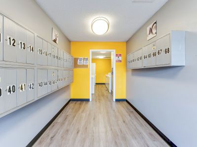 Indoor resident mailroom featuring rows of numbered silver mailboxes on neutral walls leading to a laundry area with a bright yellow accent wall at Cherry Creek apartments in Memphis.