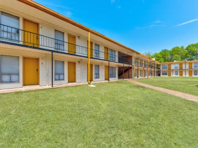 Two-story apartment buildings with white siding, black railings, and signature yellow doors surrounding a sunny green courtyard lawn at Cherry Creek apartments in Memphis.