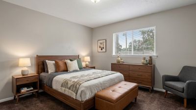 Staged primary bedroom showcasing mid-century modern wooden furniture, a leather storage bench, and deep brown carpeting at Cherry Creek apartments in Memphis.