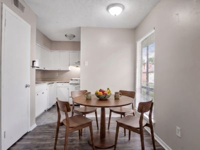 Staged dining area featuring a round wooden table and matching chairs on wood-style flooring adjacent to the kitchen at Cherry Creek apartments in Memphis.