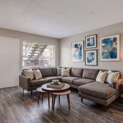 Virtually staged living room layout with a large grey sectional sofa, nesting coffee tables, and blue abstract wall art at Cherry Creek apartments in Memphis.