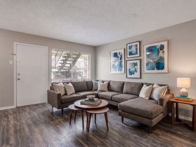 Virtually staged living room layout with a large grey sectional sofa, nesting coffee tables, and blue abstract wall art at Cherry Creek apartments in Memphis.