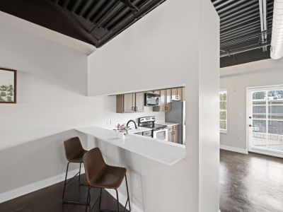 Modern kitchen breakfast bar with white countertops and brown leather barstools under an industrial ceiling at the Lofts in Town Square loft apartments in Southaven.