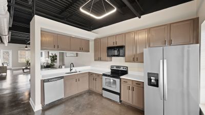 Modern kitchen with stainless steel appliances, brown wood cabinets, a geometric light fixture, and stained concrete floors at the Lofts in Town Square in Southaven.