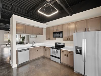 Modern kitchen with stainless steel appliances, brown wood cabinets, a geometric light fixture, and stained concrete floors at the Lofts in Town Square in Southaven.