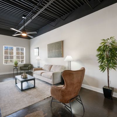 Stylish loft living room layout featuring a neutral sofa, brown accent chair, and large windows at the Lofts in Town Square loft apartments in Southaven.