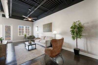 Stylish loft living room layout featuring a neutral sofa, brown accent chair, and large windows at the Lofts in Town Square loft apartments in Southaven.