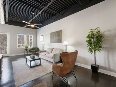 Stylish loft living room layout featuring a neutral sofa, brown accent chair, and large windows at the Lofts in Town Square loft apartments in Southaven.