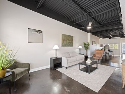 Full view of a decorated living room with a green velvet armchair, a beige sofa, and dark stained concrete floors at the Lofts in Town Square loft apartments in Southaven.