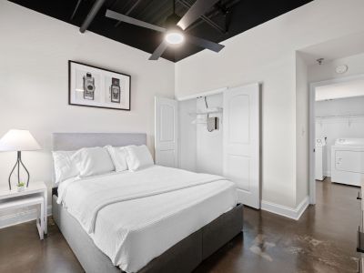 Contemporary loft bedroom featuring a grey upholstered bed, an industrial black ceiling with a fan, and polished concrete floors at the Lofts in Town Square in Southaven.