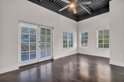 Bright, empty loft apartment living area showcasing high industrial ceilings, dark concrete floors, and double glass doors opening to a balcony at the Lofts in Town Square in Southaven.