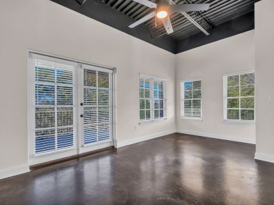 Bright, empty loft apartment living area showcasing high industrial ceilings, dark concrete floors, and double glass doors opening to a balcony at the Lofts in Town Square in Southaven.