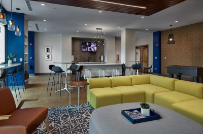 Modern resident clubhouse lounge featuring a lime green sectional sofa, high-top tables, and a foosball table at Madison@McLean Midtown apartments in Memphis.