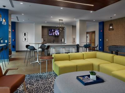 Modern resident clubhouse lounge featuring a lime green sectional sofa, high-top tables, and a foosball table at Madison@McLean Midtown apartments in Memphis.