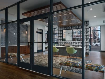 Main leasing office reception area viewed through glass doors, featuring stylized icon wallpaper and modern seating at Madison@McLean Midtown apartments in Memphis.